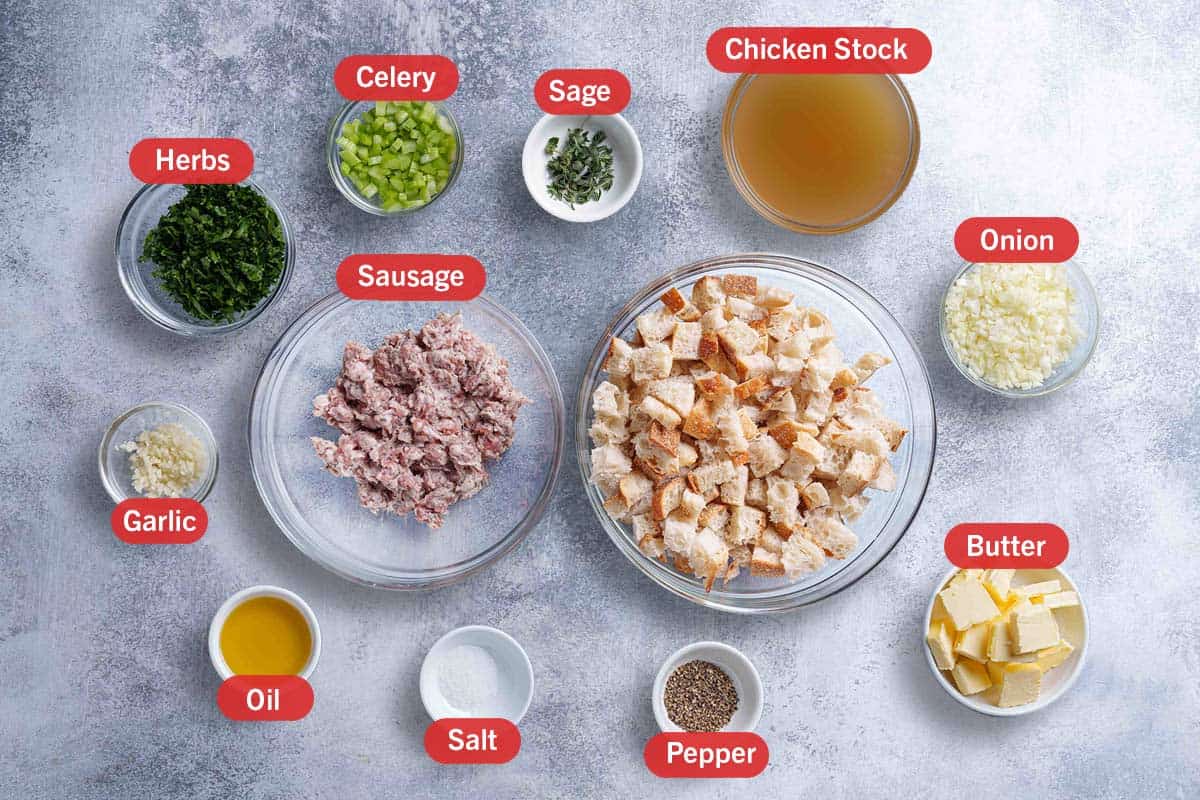 Image of all the ingredients needed to prepare the sausage meat stuffing: herbs, celery, sage, chicken stock, garlic, sausage, onion, oil, salt, pepper, butter, diced bread.