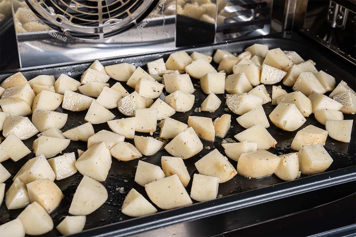Potatoes arranged on a baking tray being placed into the oven for roasting.