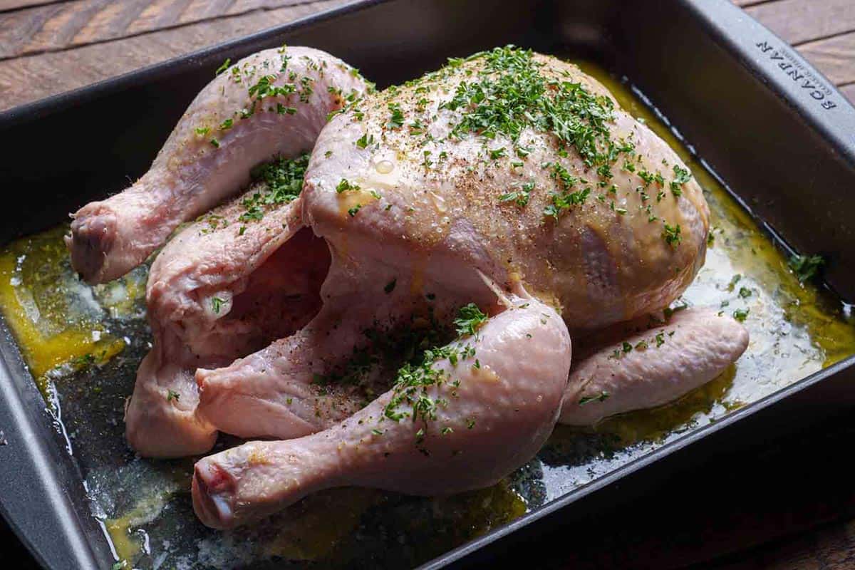 Image of the chicken being seasoned and buttered, including under the skin and inside the cavity.