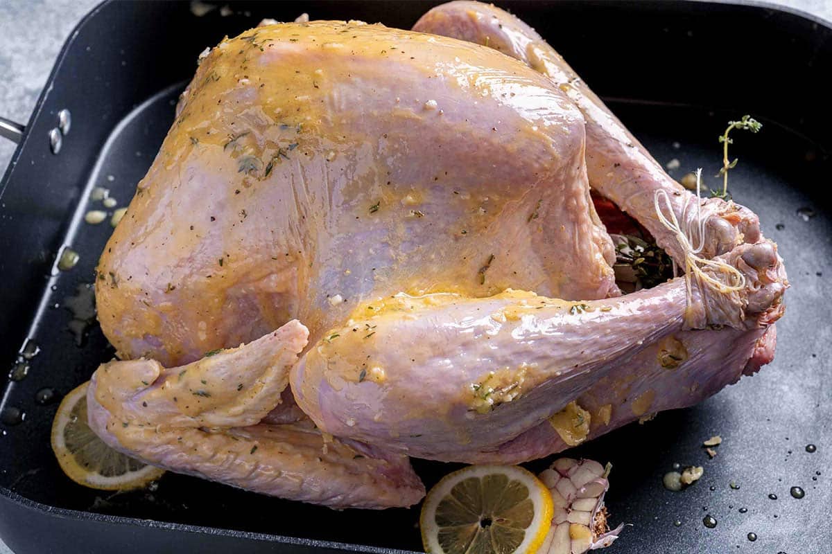 moist turkey bathed in herb butter mixture in a dish with garlic and lemon