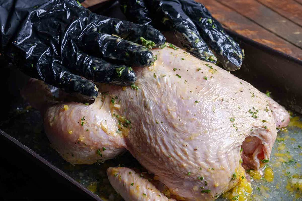 Image showing minced garlic being rubbed over the chicken, with ingredients mixed over and under the skin.