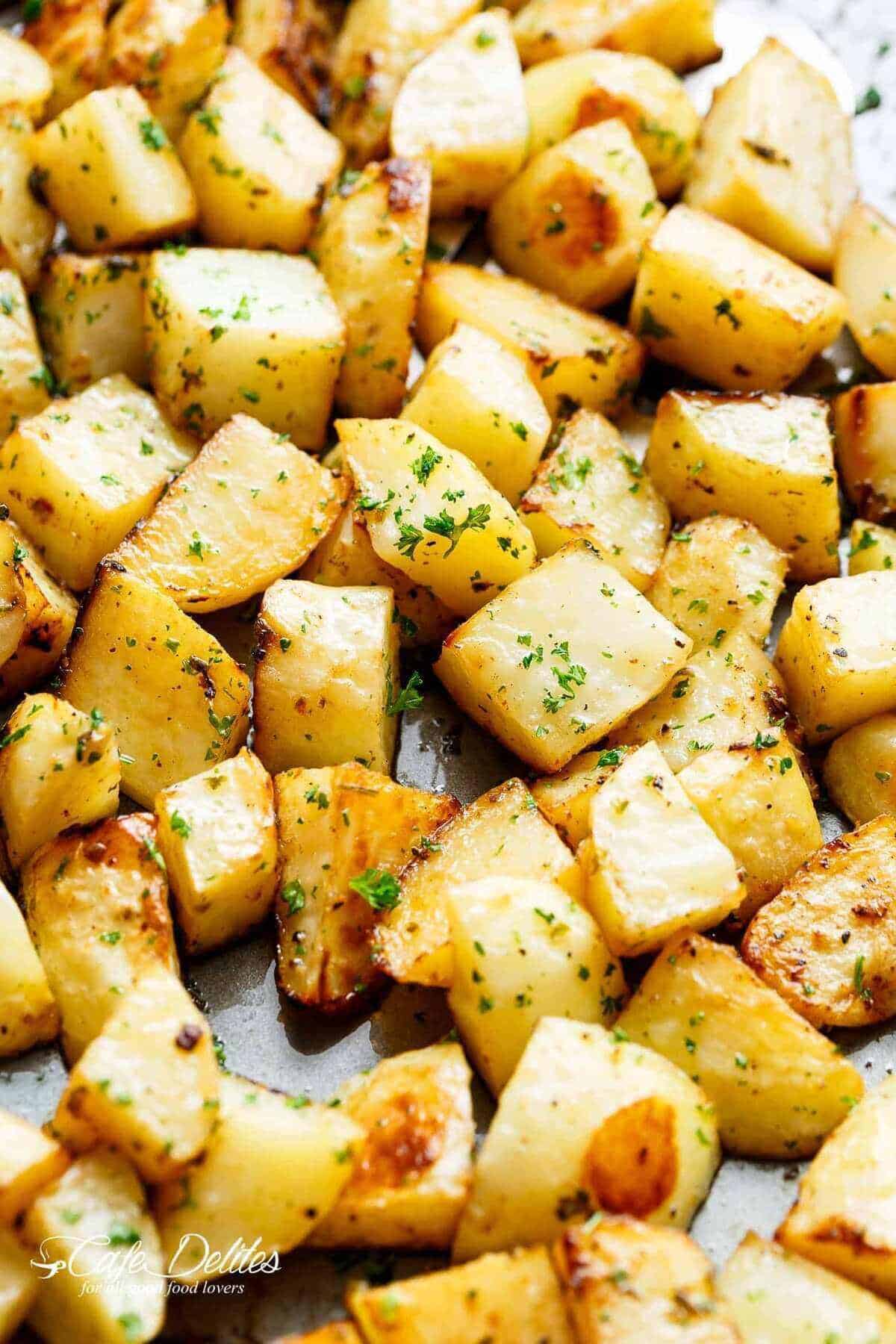 Yummy Crispy garlic roasted potatoes sprinkled with fresh green herbs on a baking tray.