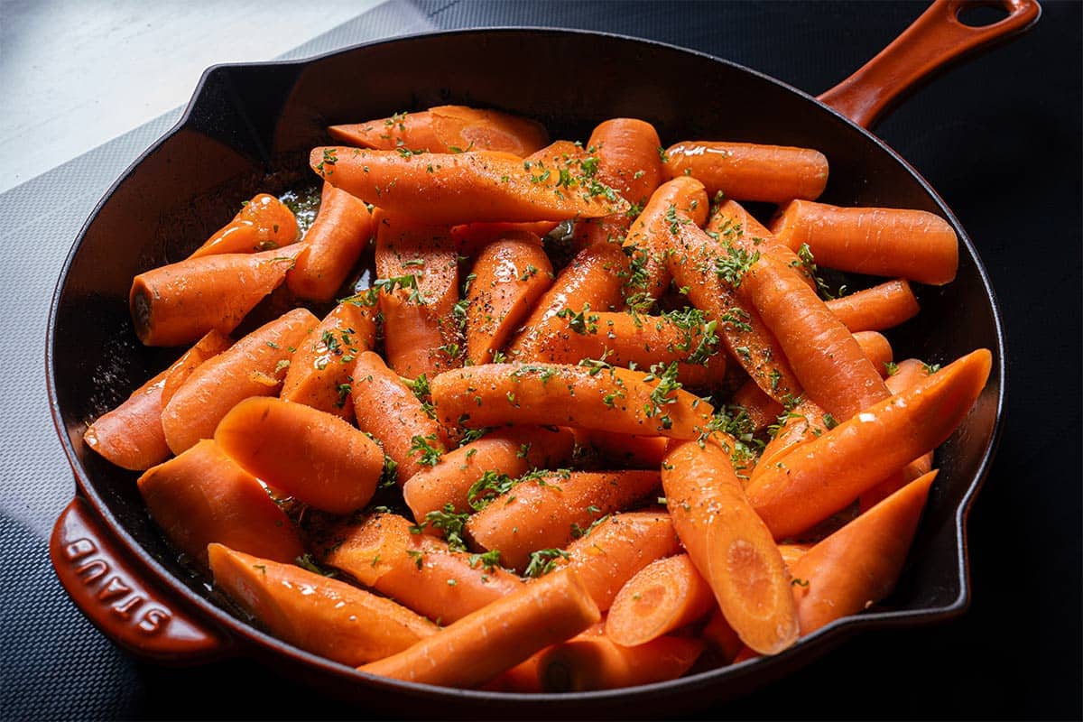 Image of carrots being placed in a pan and tossed in the thickening sauce.