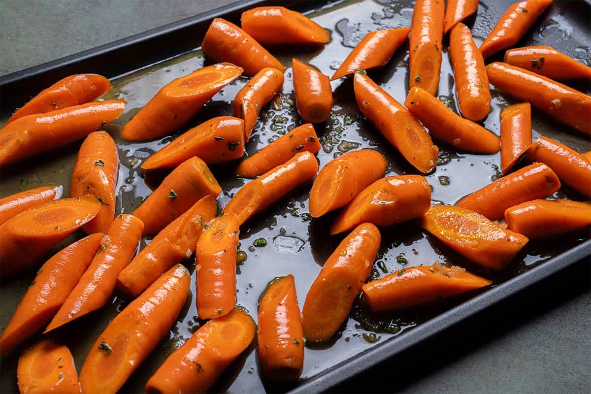 Image of carrots being laid on a baking tray, ready to be put into the oven.