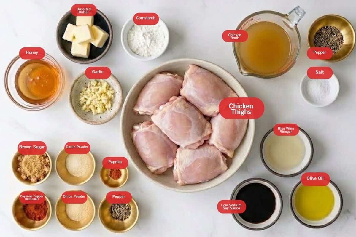 Flat lay photo of ingredient shot of honey, unsalted butter, cornstarch, chicken broth, pepper, salt, rice wine vinegar, olive oil, low sodium soy sauce, chicken thighs, onion and garlic powder, paprika, brown sugar, cayenne powder (optional) to make a slow cooker honey garlic chicken.