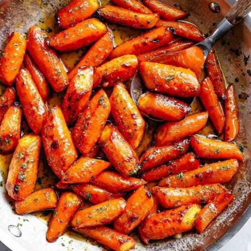 Close-up image of delicious butter-roasted carrots in a pan, garnished with fresh parsley.