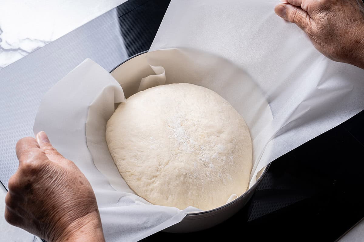 An image of the bread dough being transferred into the Dutch oven while still resting on parchment paper.