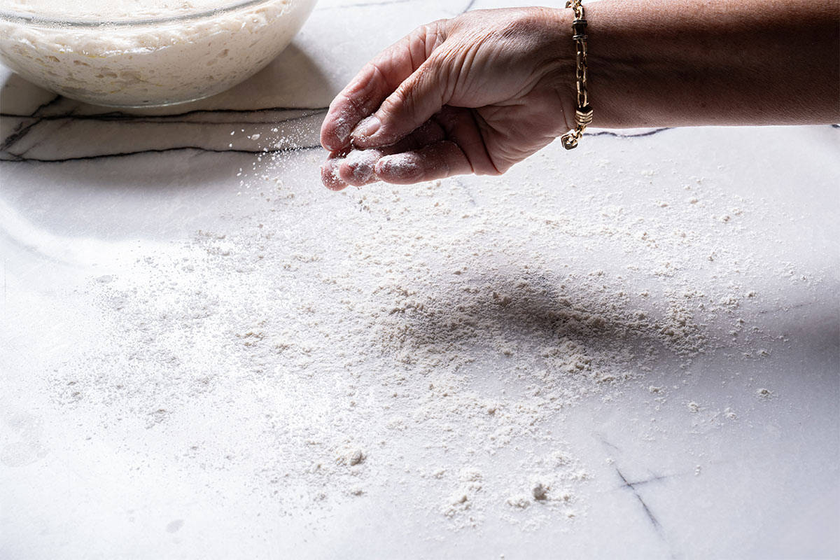 A surface being lightly floured by a hand.