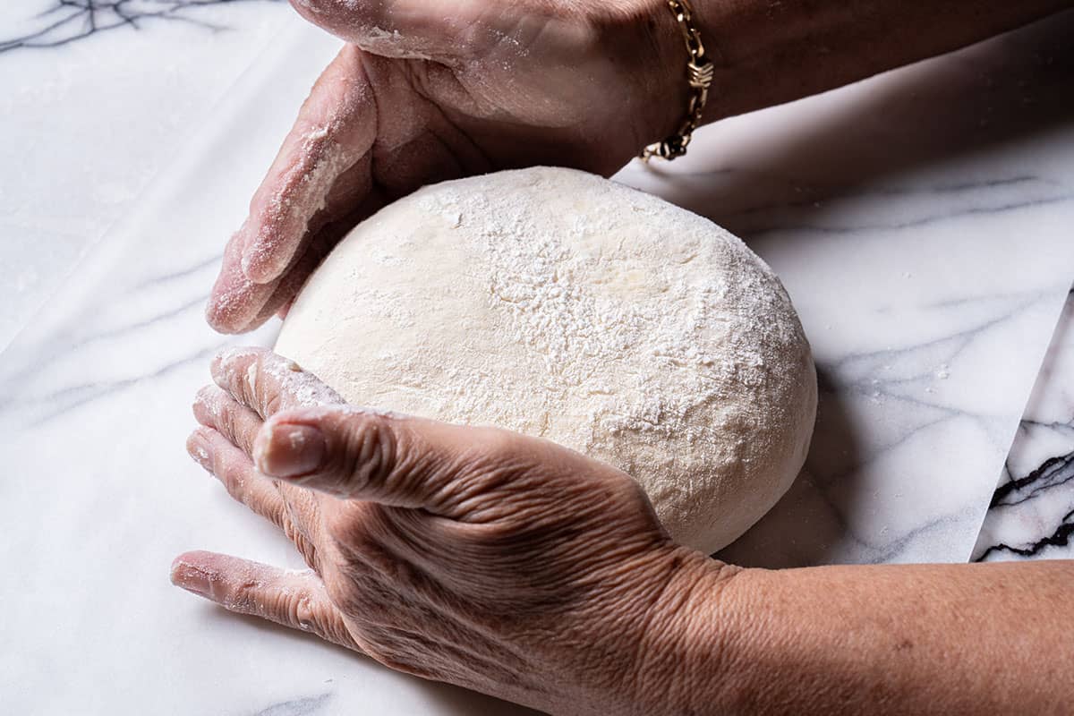 Image of hands moving the round bread dough onto parachment paper.