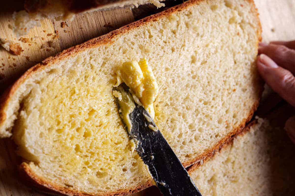 An image of a knife spreading butter over sliced warm bread.