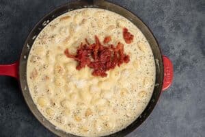 adding sun-dried tomatoes to the sauce with parmesan