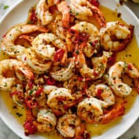 A pile of shrimp on a white plate sitting in chili garlic butter sauce. Served with broken bread pieces.