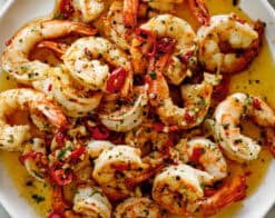 A pile of shrimp on a white plate sitting in chili garlic butter sauce. Served with broken bread pieces.