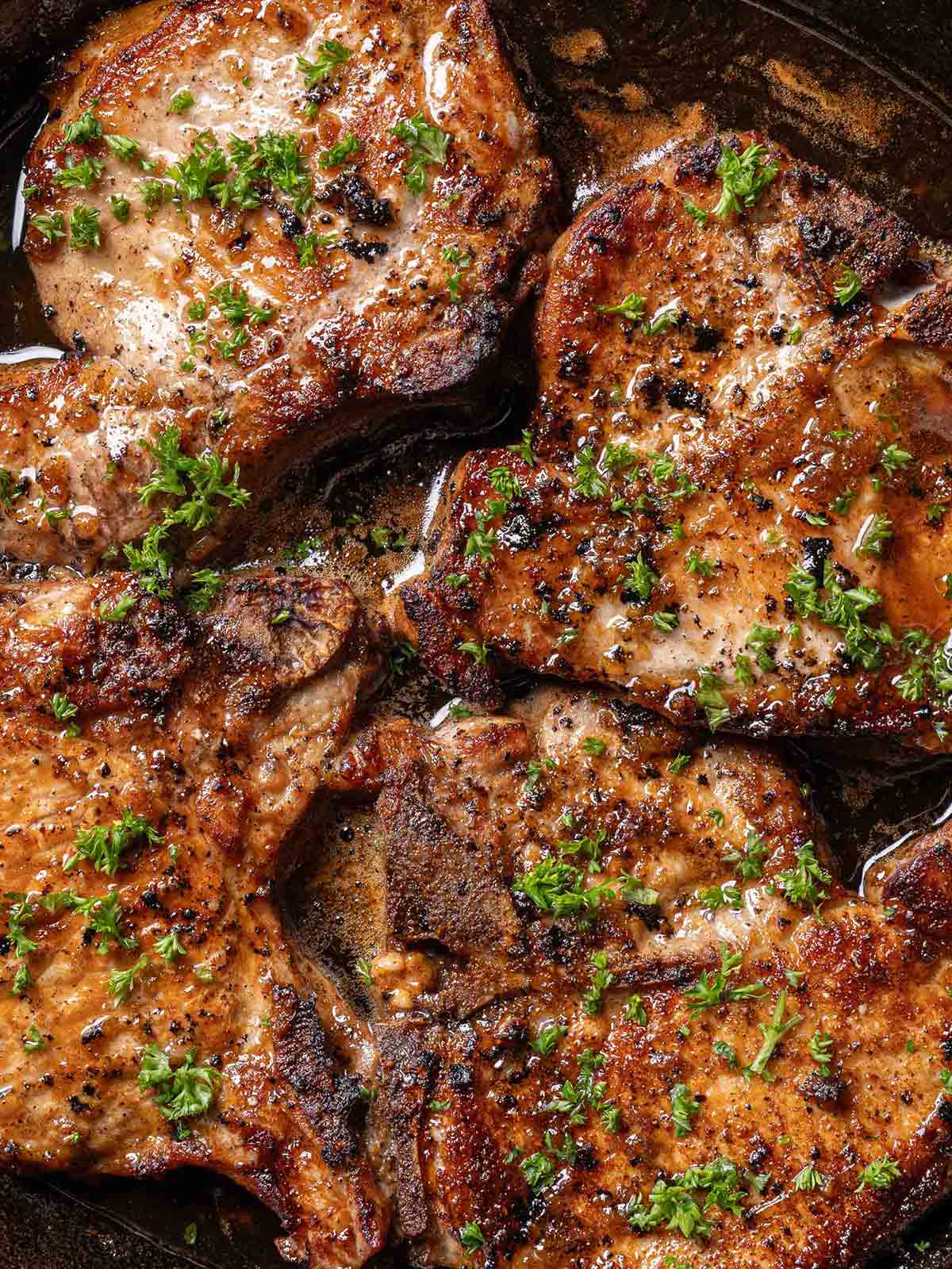 finished juicy honey garlic pork chops in a black pan garnished with parsley