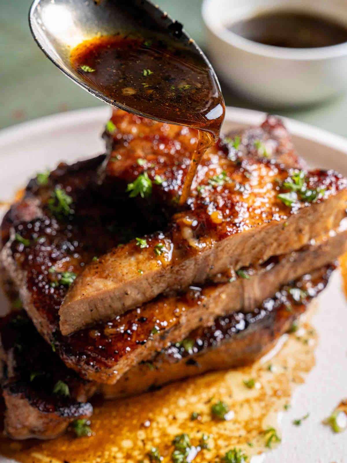 A stack of Hot and spicy pork chops smothered in honey garlic sauce with a silver spoon pouring sauce on top.