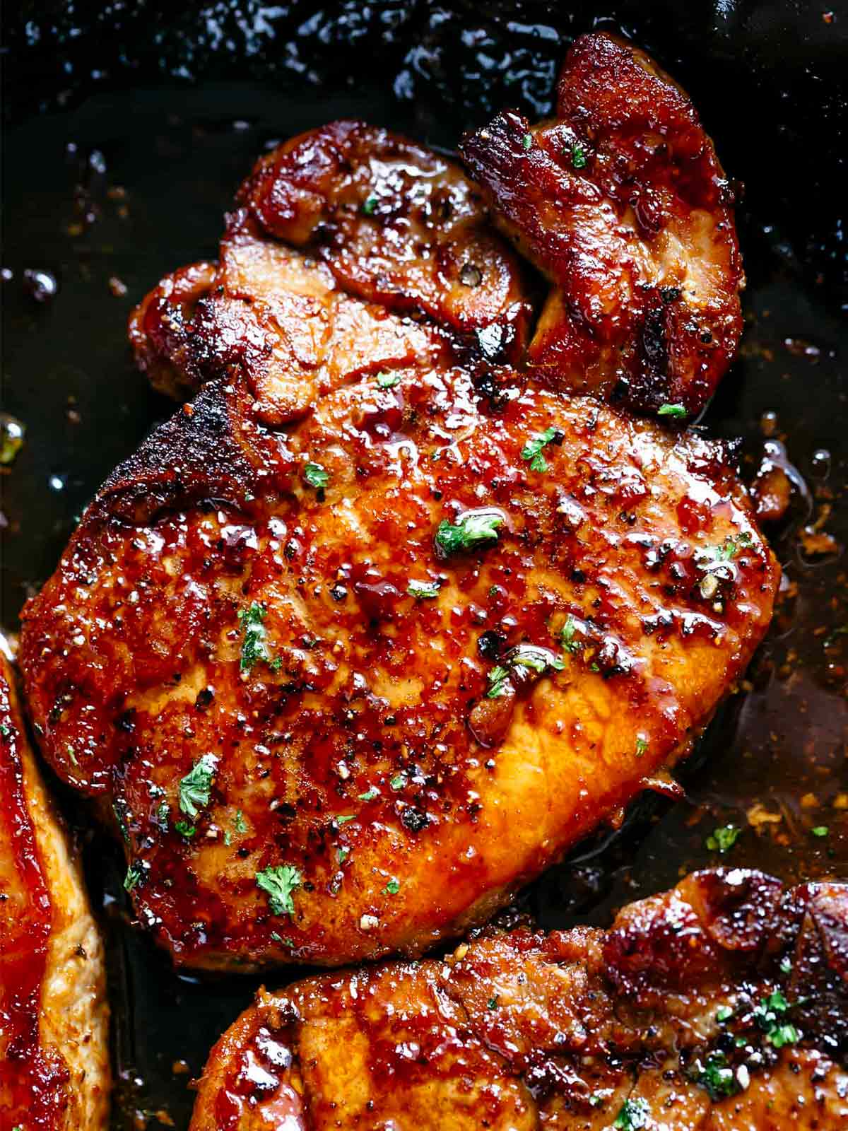 finished juicy honey garlic pork chops in a black pan garnished with parsley
