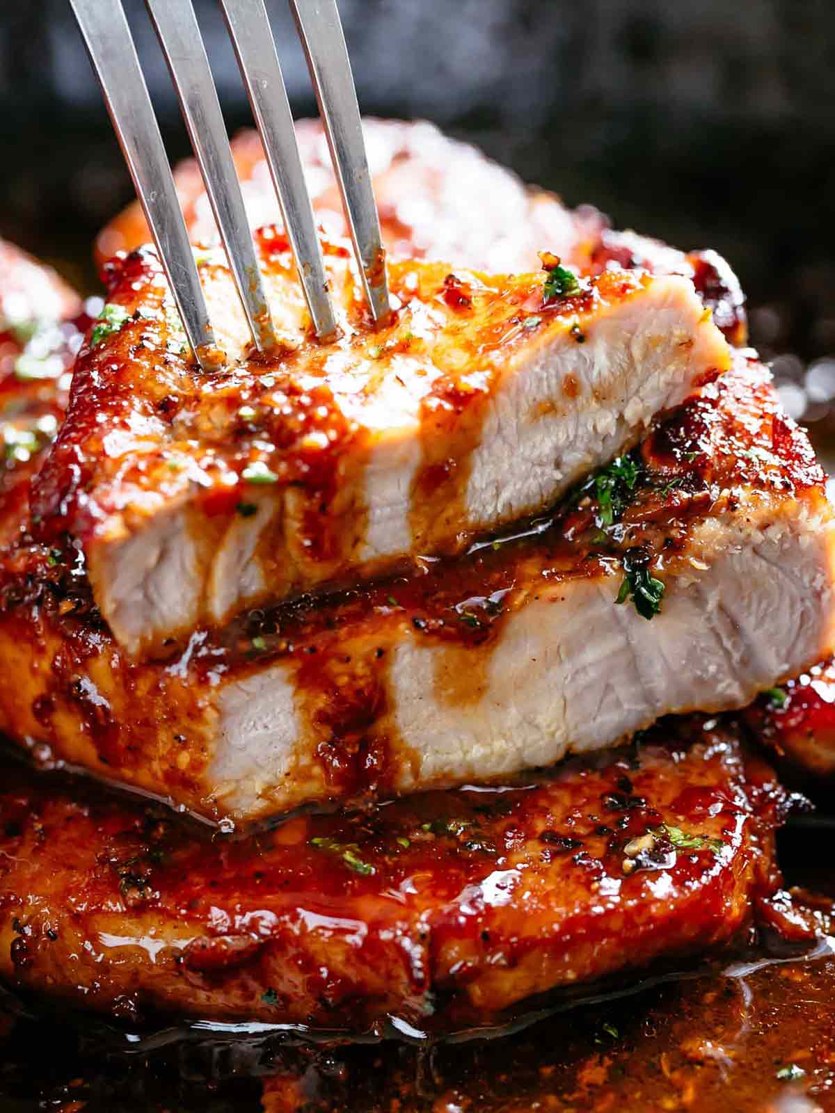 A stack of Hot and spicy pork chops smothered in honey garlic sauce with a silver spoon pouring sauce on top.