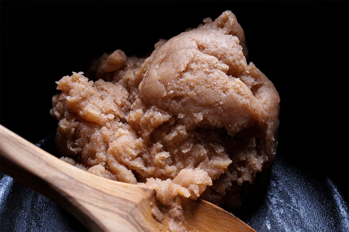 An image depicting water, sugar, vanilla, cinnamon, and salt being heated with butter in a medium-sized saucepan.