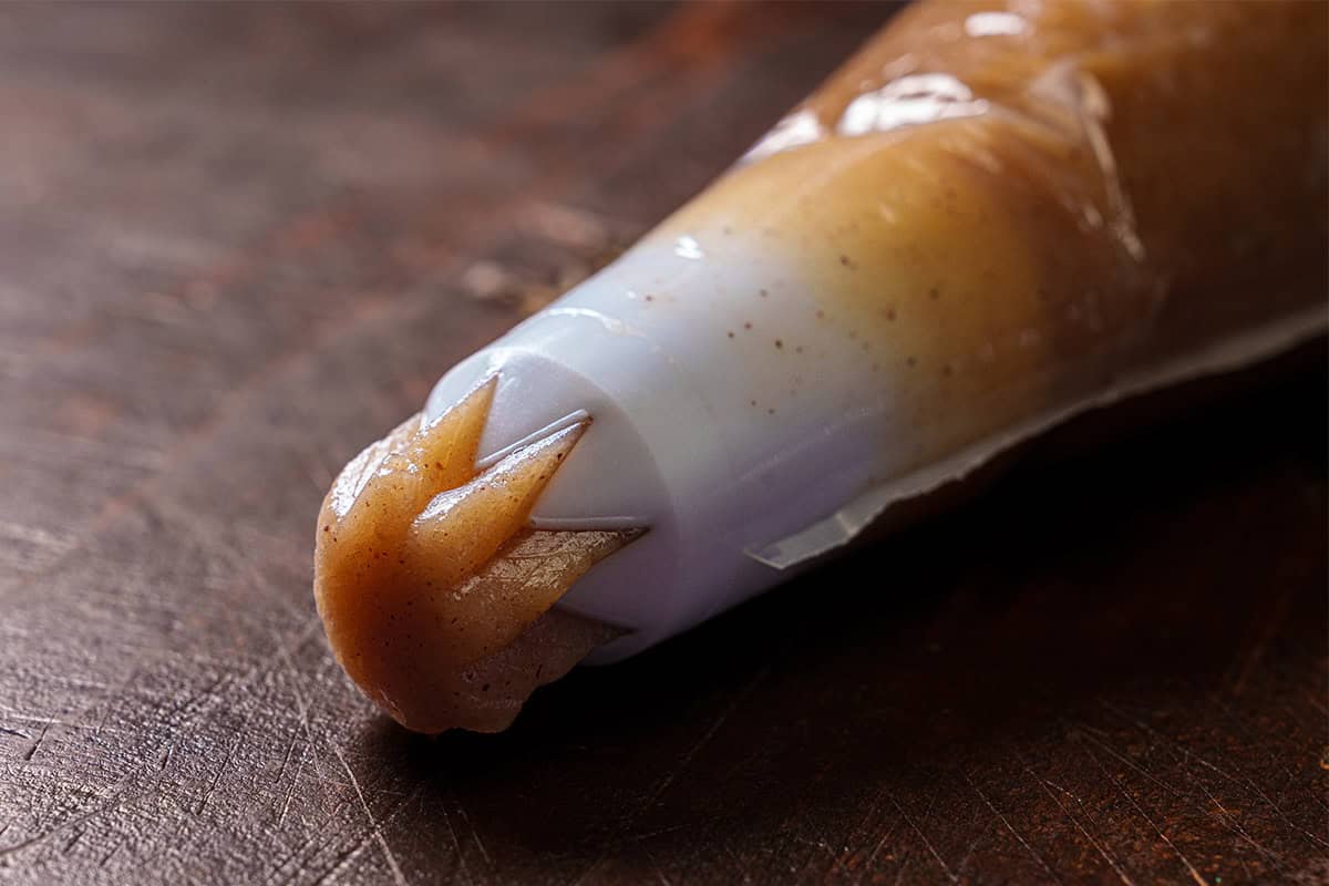 Close-up image of a pastry bag with churro dough gently spilling out of it.