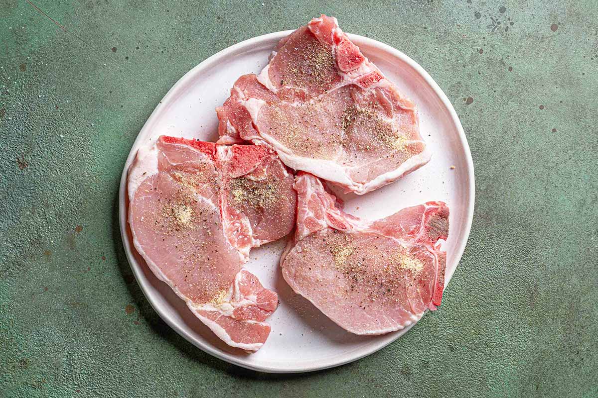 pork chops on a white plate witha green textured background wseasoned with salt and pepper