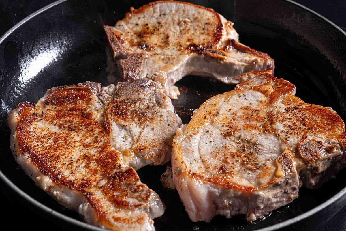 brown, seared pork chops sizzling in a pan