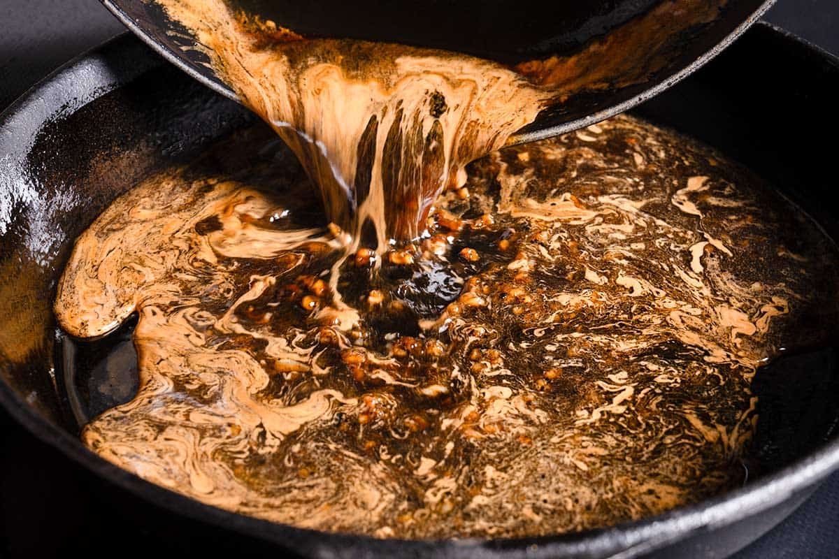 honey garlic sauce being poured from a bowl to a pan with browned bits from seared pork chops