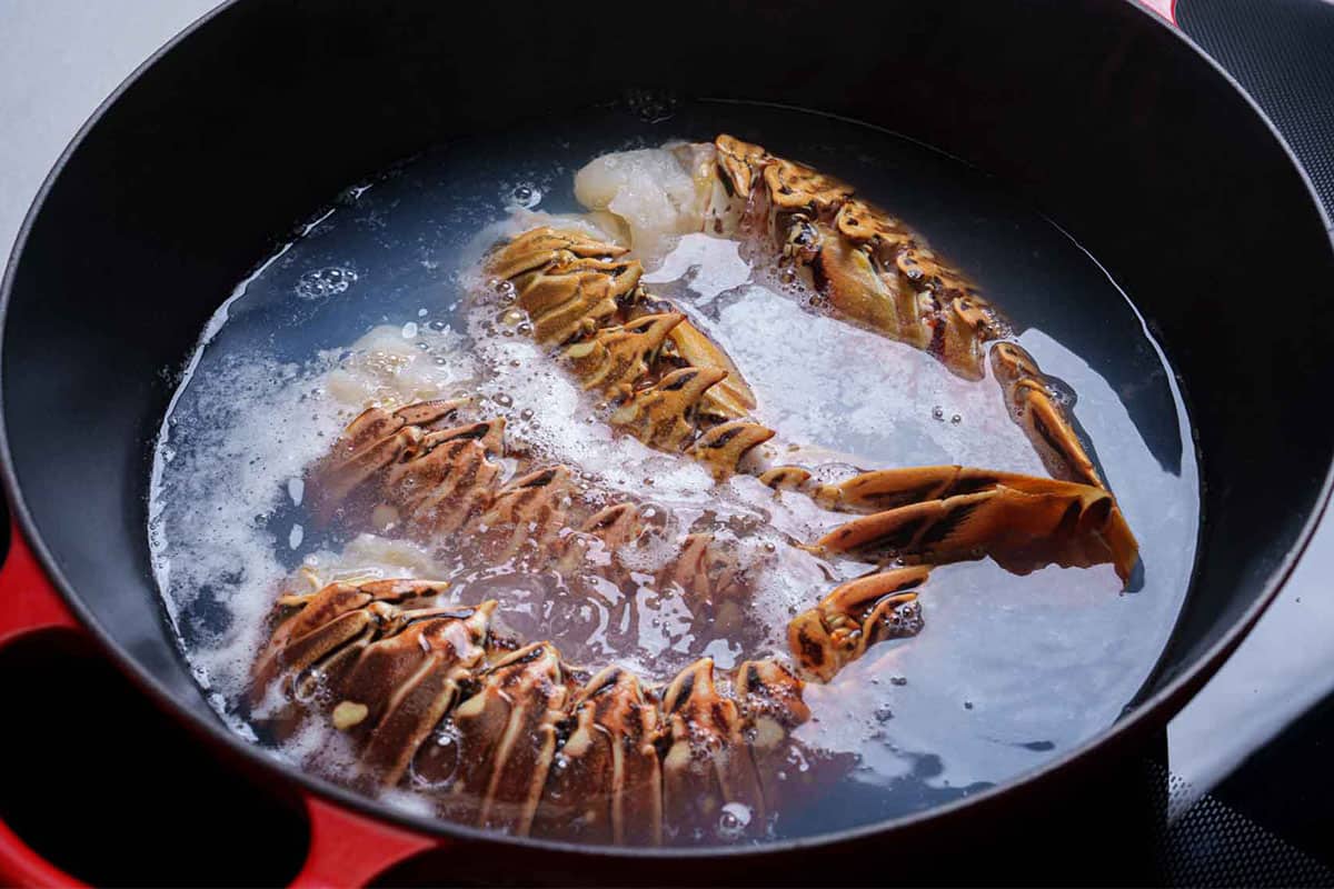 Lobster tails being boiled in a pan with a dash of salt.