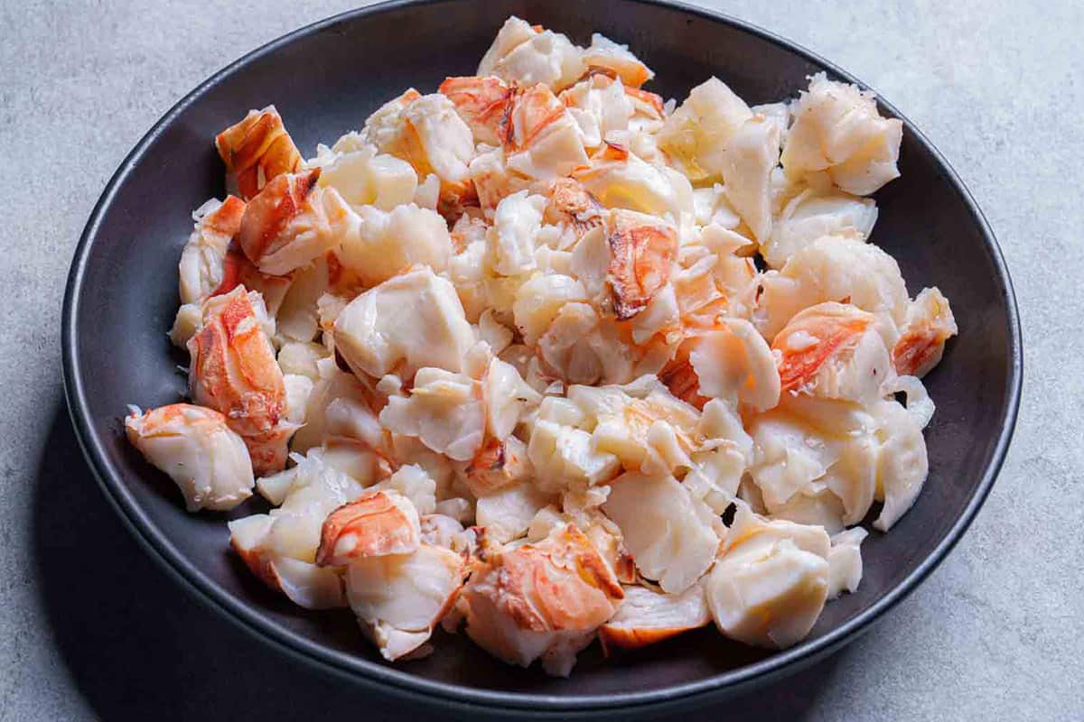 Chopped up lobster meat in a black bowl.