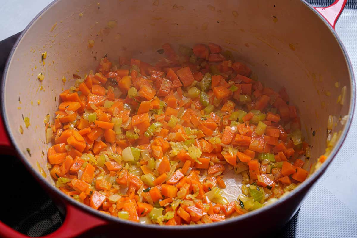 Vegetables being sautéed in a pan until soft.