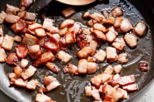 Bacon frying in a black pan with a wooden spoon