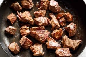 Seared beef pieces in bacon grease in a black pan