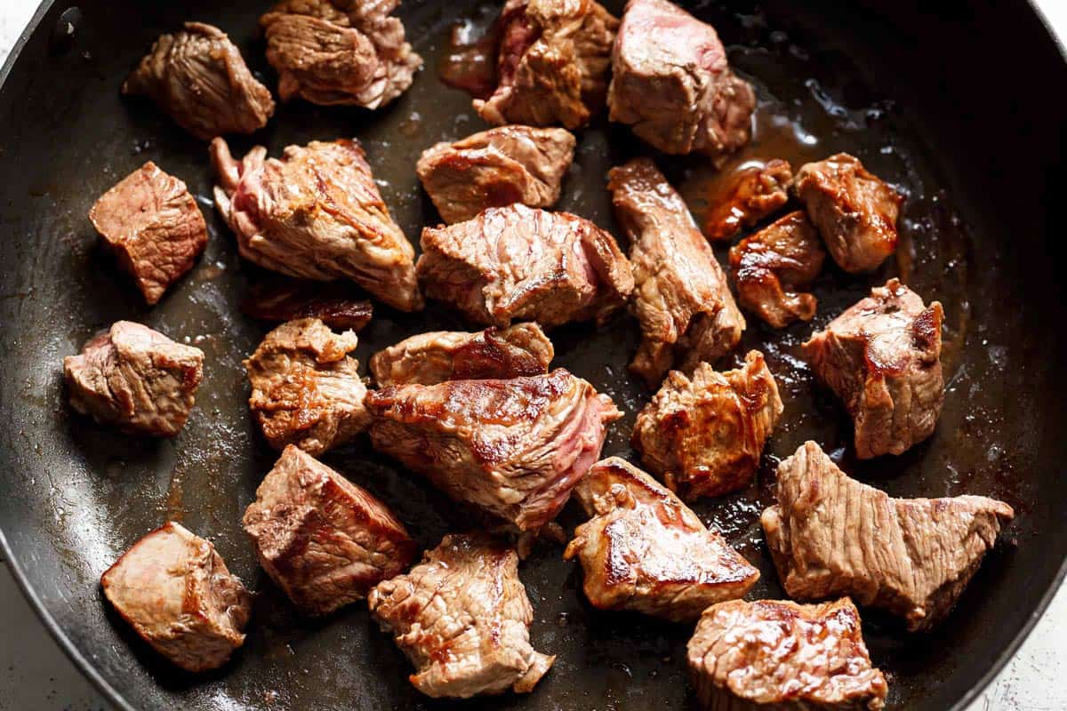 Seared beef pieces in bacon grease in a black pan
