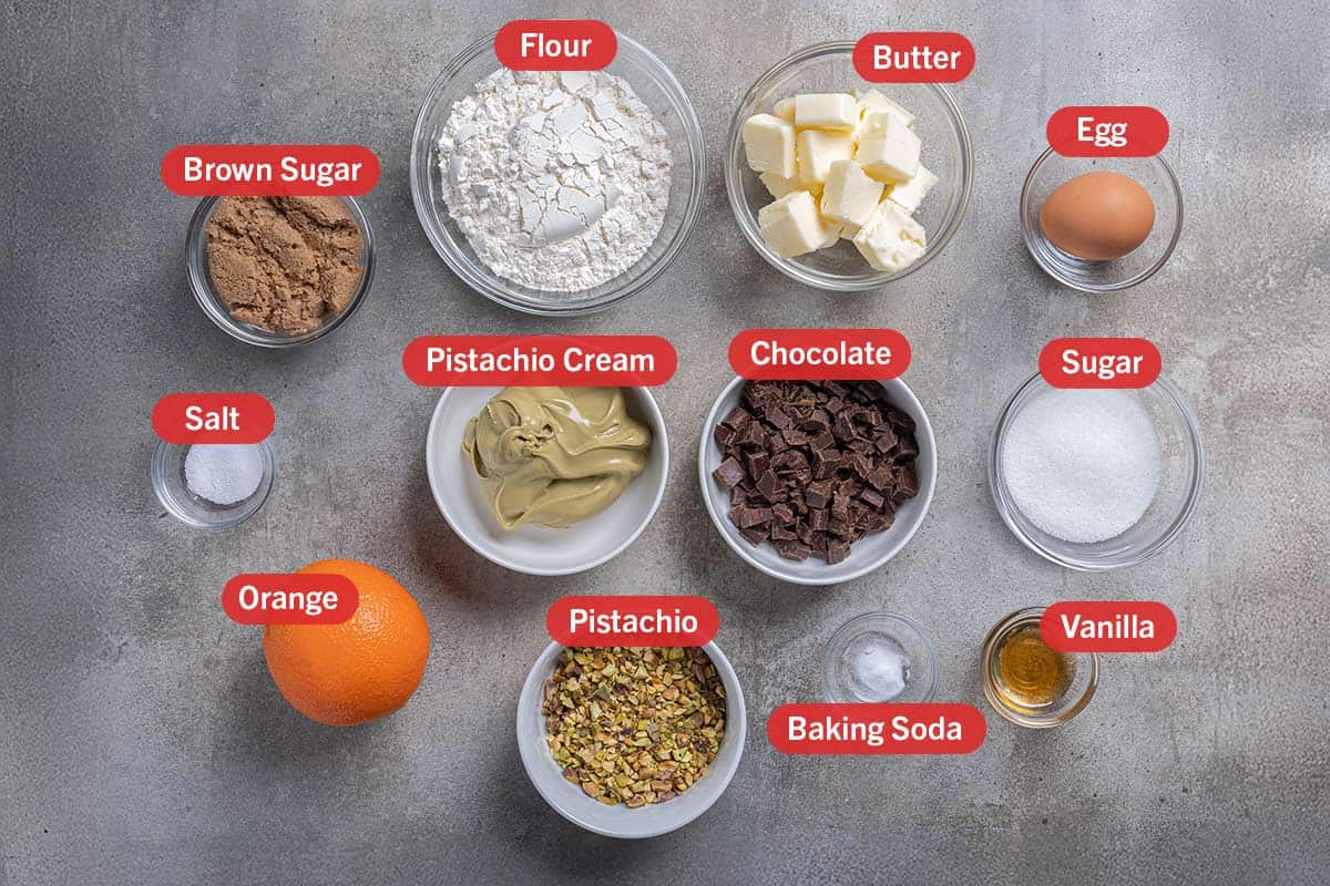 Ima of the ingredients needed for the creation of this recipe, specifically: pistachio cream, chocolate, sugar, vanilla, baking soda, pistachio, orange, salt, brown sugar, flour, and butter.