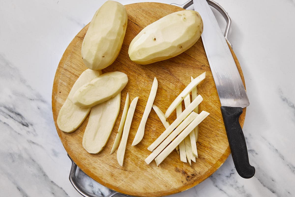 potatoes cut into fries strips on a cutting board