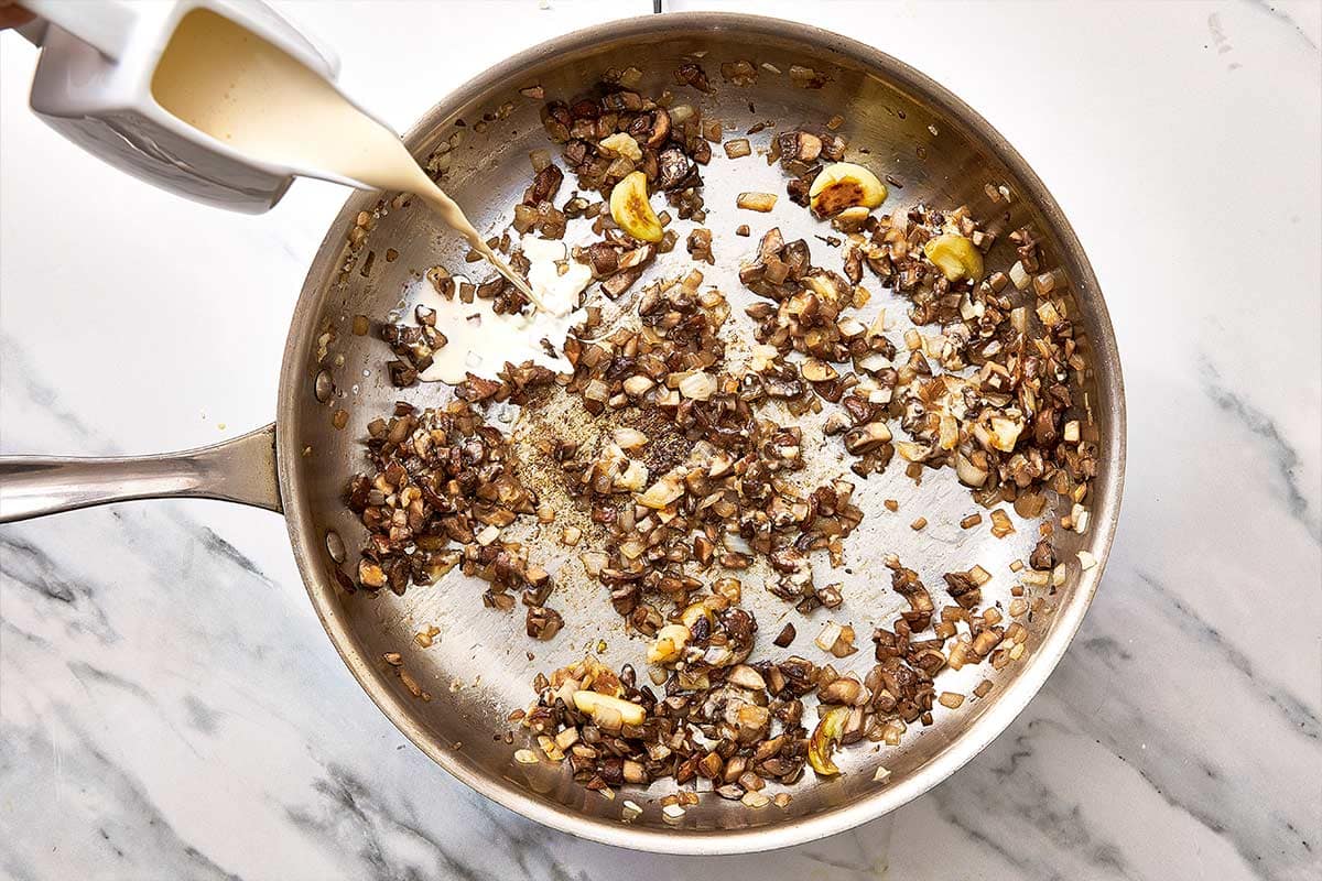 mushrooms, onion and garlic seared in a pan with cream being poured in