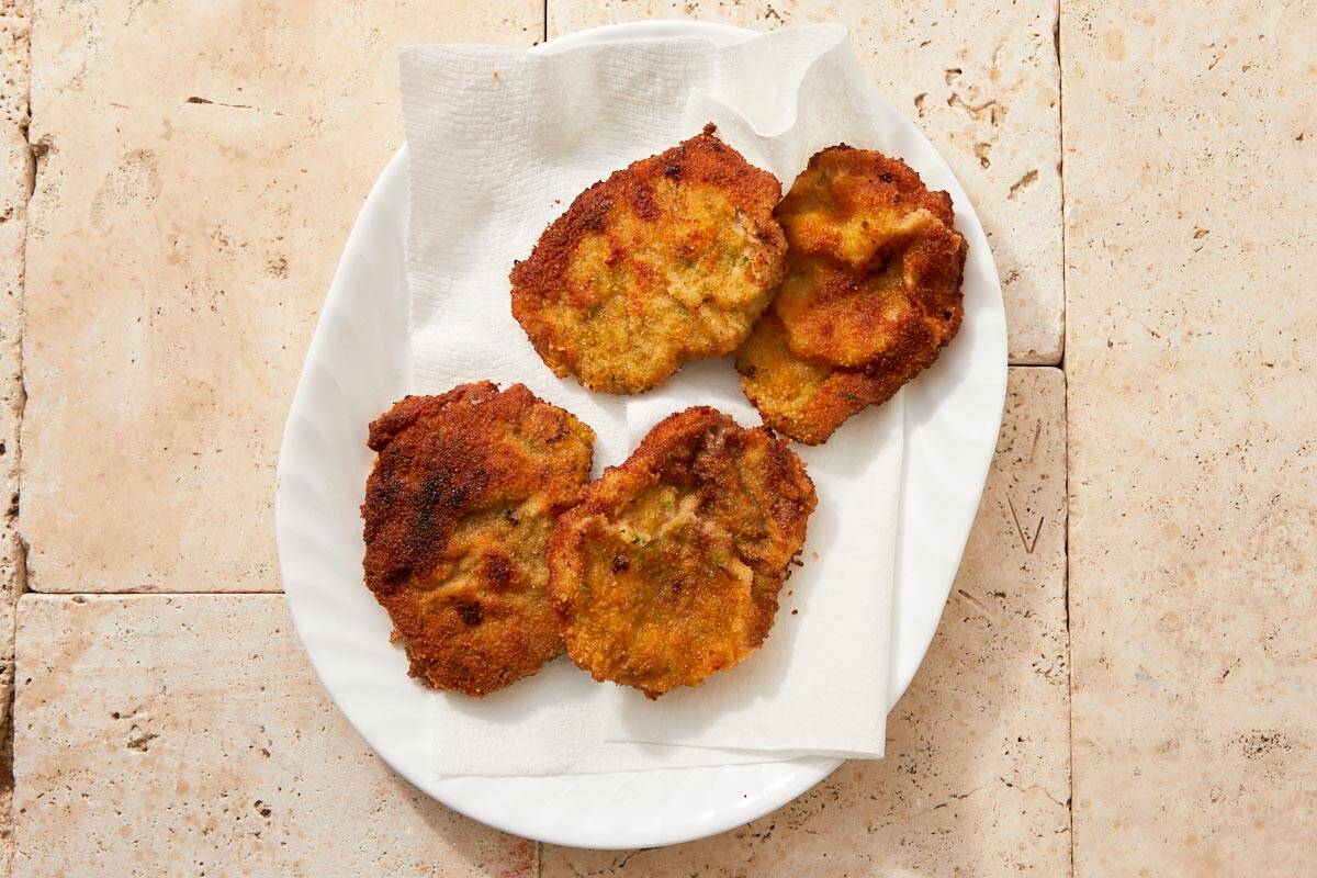 Freshly fried beef schnitzels resting on a paper towel-lined plate.