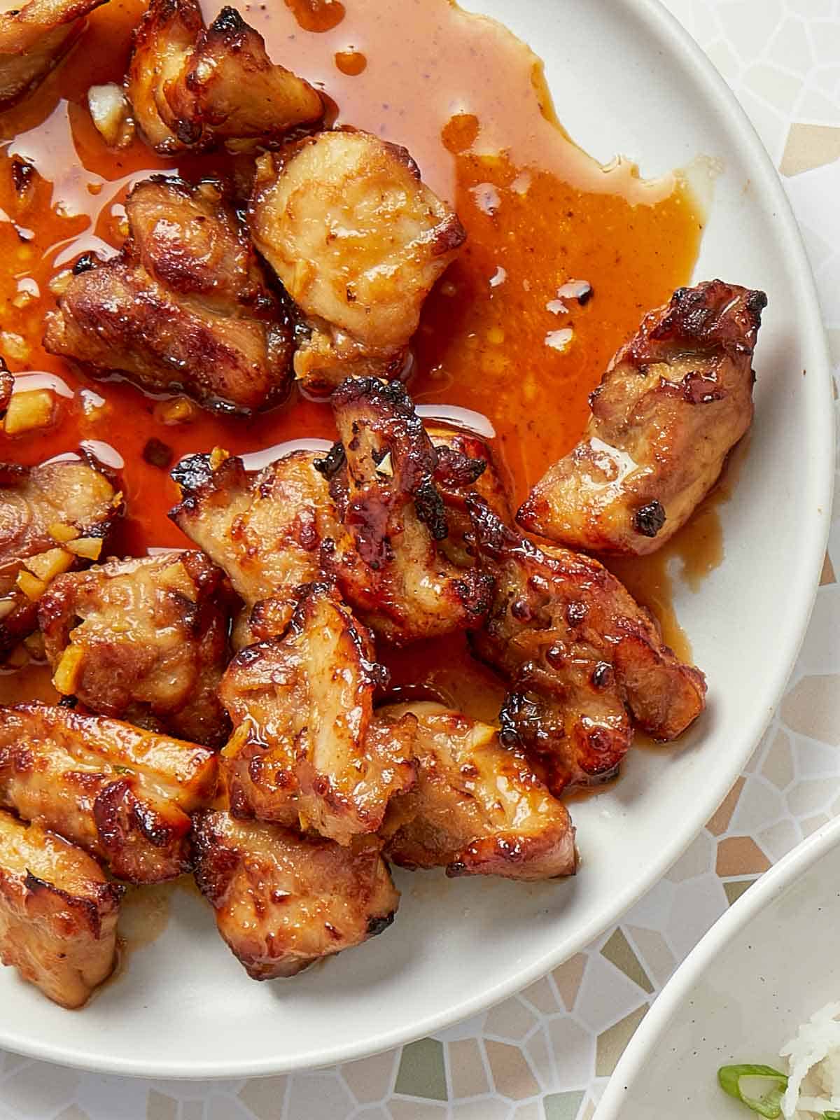 Close-up of crispy air fryer teriyaki chicken glazed with a glossy, garlicky sauce on a white plate