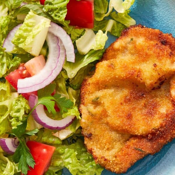 Crispy beef milanesa served with fresh tomato salad and greens on a white plate