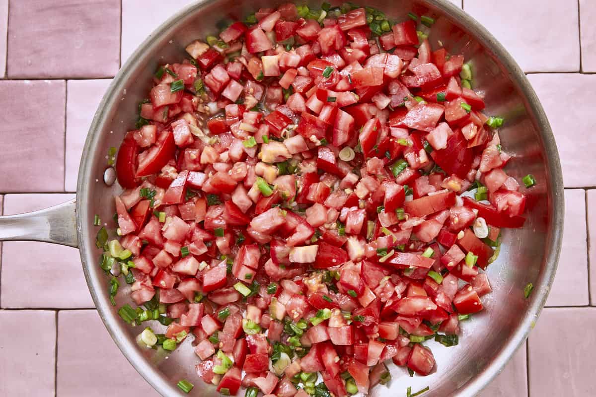 Chopped tomatoes and green onions cooking in a stainless steel pan.