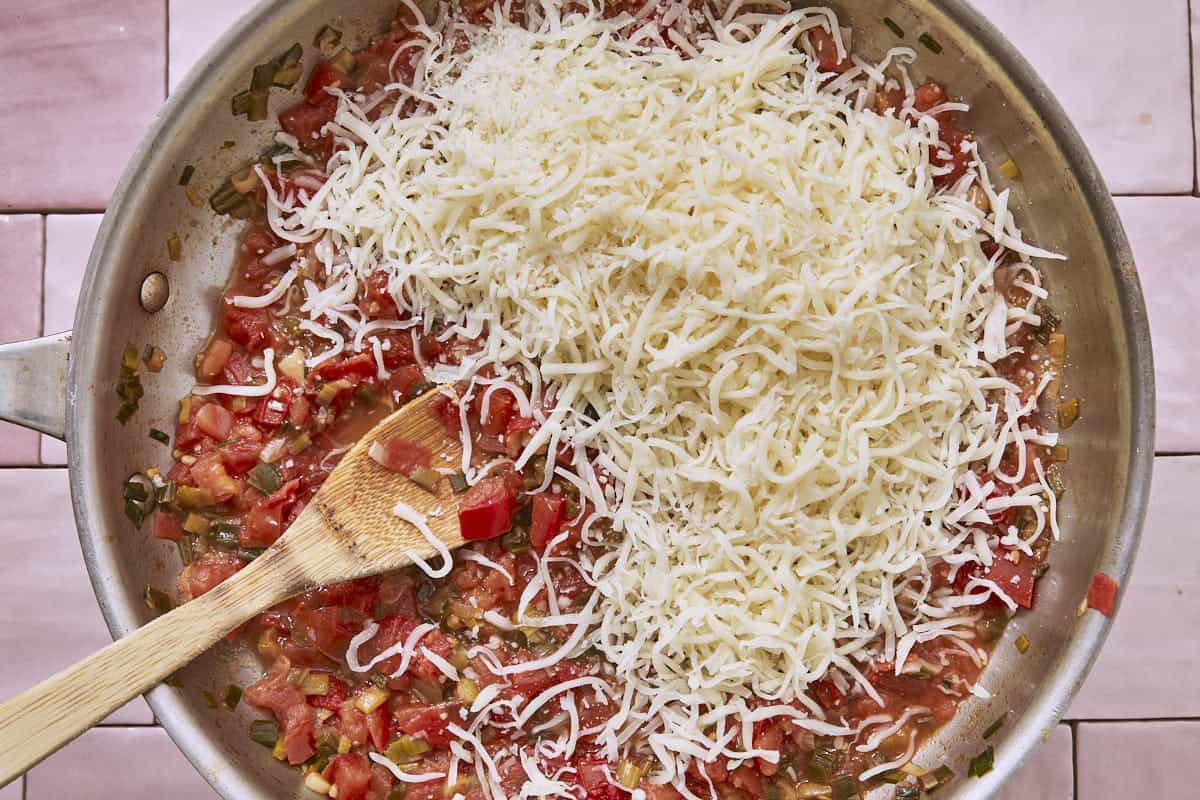 Shredded mozzarella cheese added to a simmering tomato and green onion sauce in a pan