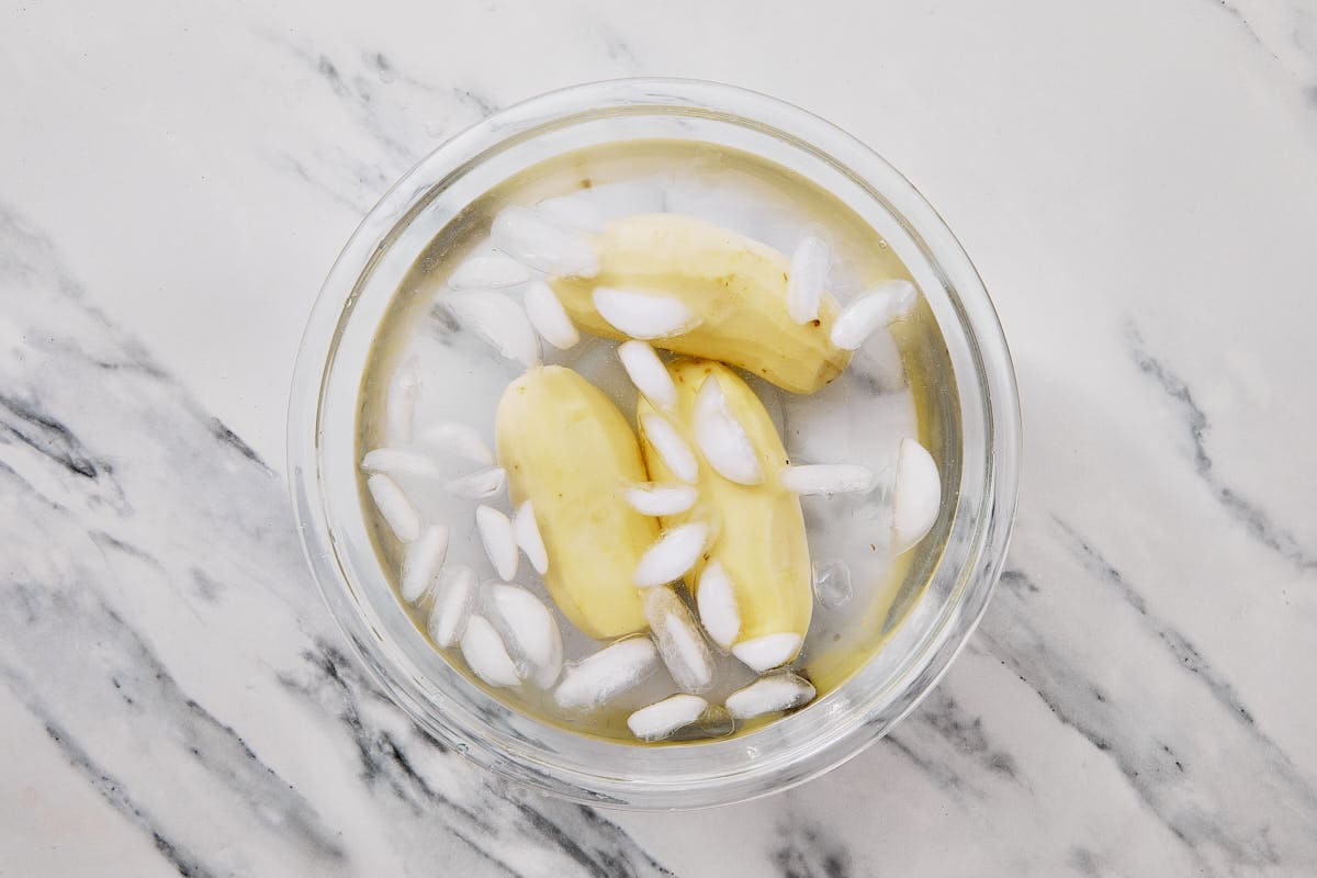 peeled potatoes in a bowl with ice and water