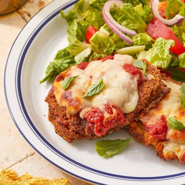 Crispy beef parmigiana topped with melted cheese and tomato sauce, served with a fresh green salad and red onion slices on a white plate.