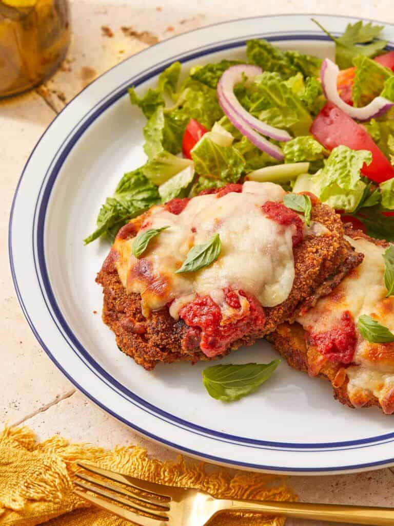Crispy beef parmigiana topped with melted cheese and tomato sauce, served with a fresh green salad and red onion slices on a white plate.