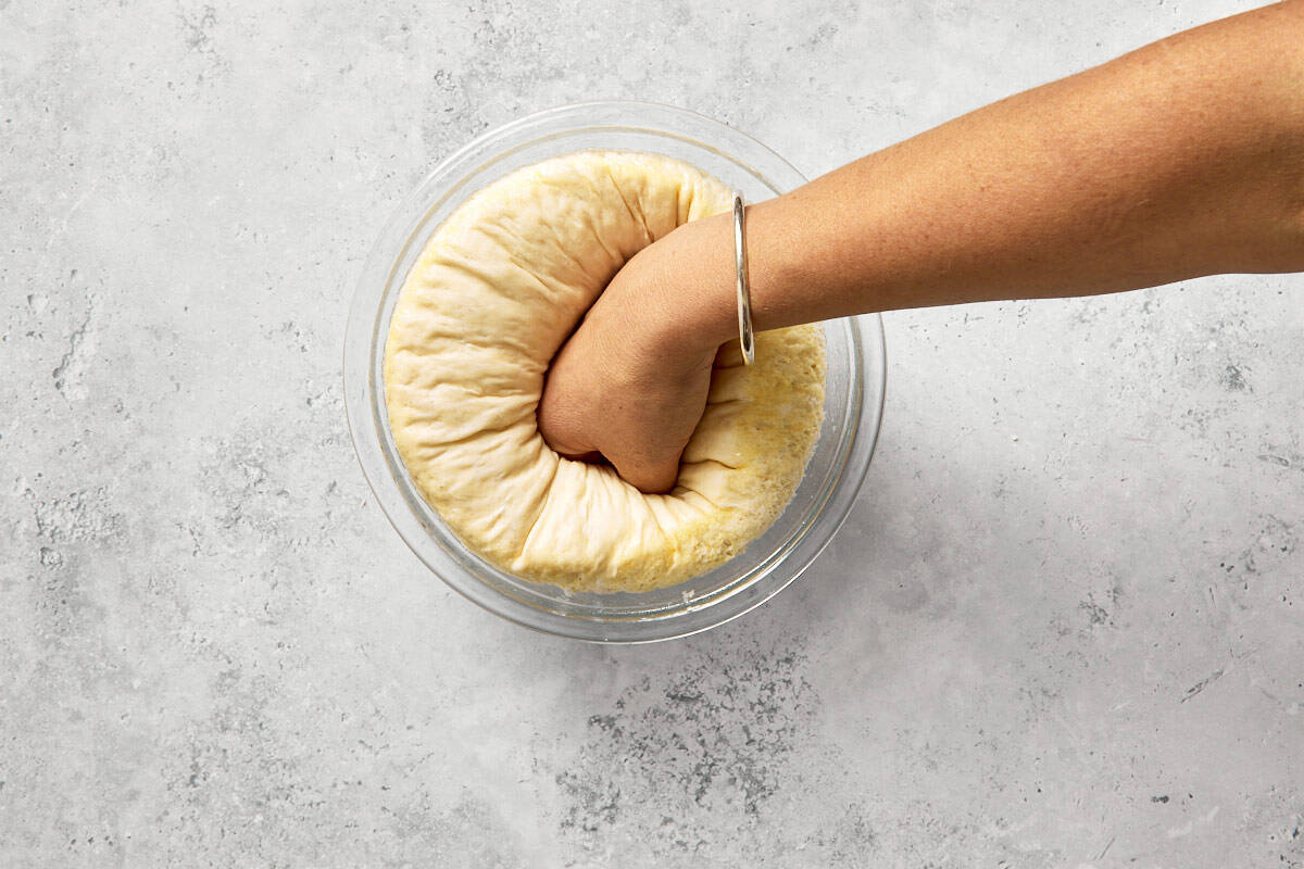 Hand punching down risen dough to release air after first proof.
