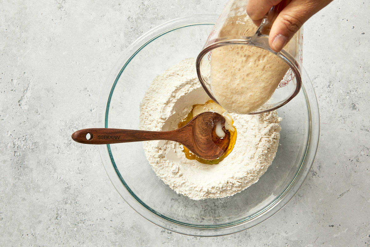 Pouring yeast into a bowl of flour and olive oil to start the Pan Coca dough.