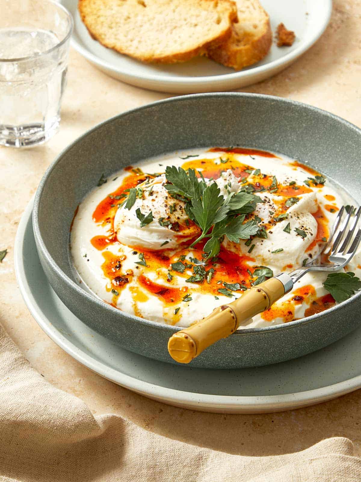Turkish eggs served in a bowl with yogurt, poached eggs, chili butter, and fresh herbs, with toasted bread on the side.