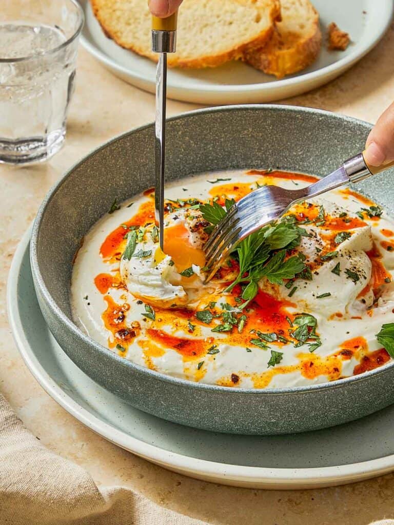 Cutting into a soft poached egg over creamy yogurt and chili butter — golden yolk, meet toasted bread.
