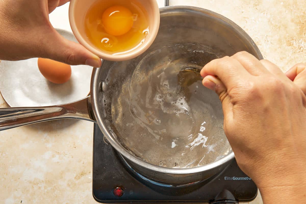 Preparing poached eggs by cracking one into simmering water.