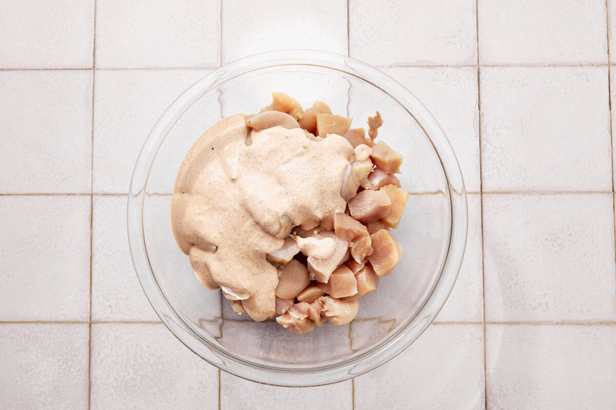 Raw chicken pieces in a glass bowl topped with cream.