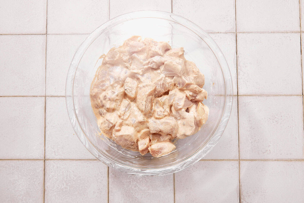 Chicken pieces marinating with plastic wrap.